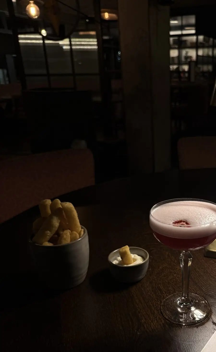 A cocktail and small bowls of snacks beside a brass lamp at The Reach Riverside bar