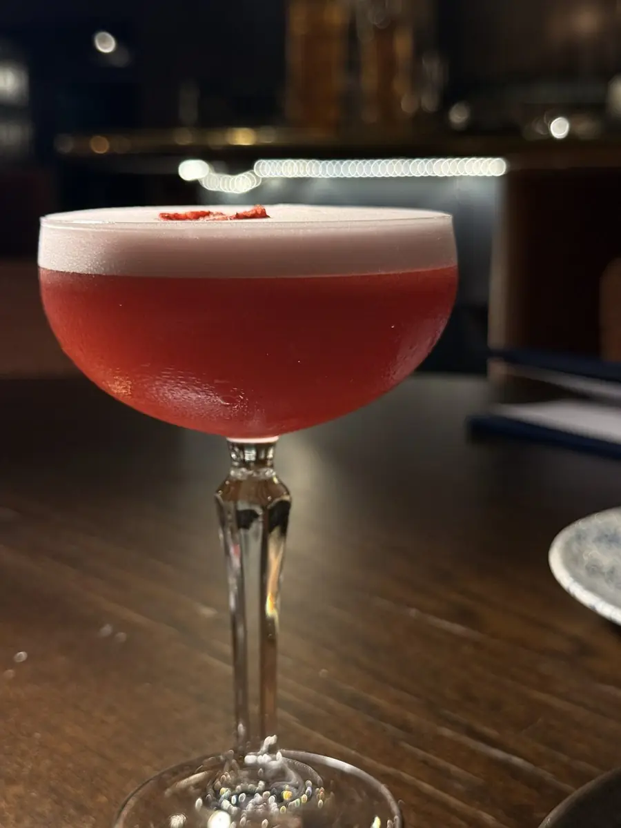 A frothy raspberry cocktail at The Reach Riverside, in a coupe glass on a dark wooden table