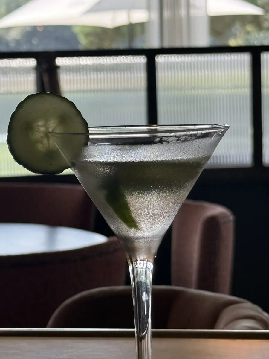 A chilled martini with a cucumber slice beside the riverside windows